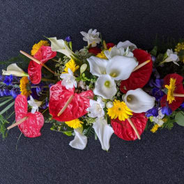 Long floral arrangement with red anthuriums, white calla lilies, and yellow daisies