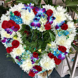 Heart-shaped floral wreath with red roses, white daisies, and blue orchids