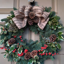 Holiday wreath with pine, holly, pinecones, and a music-note ribbon bow