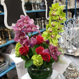 Arrangement of pink and green orchids with red roses in a glass vase