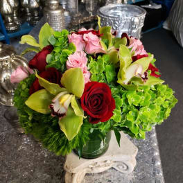 Bouquet of red roses, pink blooms, and green orchids in a glass vase