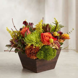 Mixed floral arrangement in a dark wooden container with orange roses and green blooms