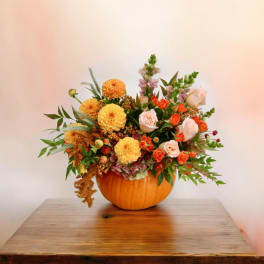 Floral arrangement in a pumpkin-shaped container with orange and peach blooms