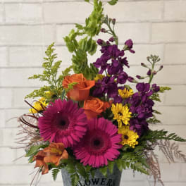Mixed bouquet in a metal bucket with pink gerberas, orange roses, and purple blooms