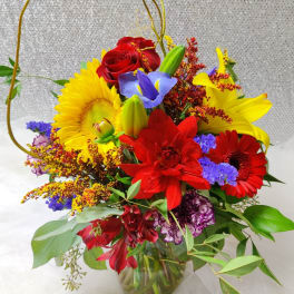 Bright mixed bouquet with red roses, sunflowers, and lilies in a glass vase