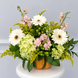 Flower arrangement in a pumpkin container with white daisies and pink blooms