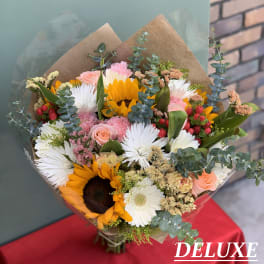 Mixed bouquet with sunflowers, white daisies, and pink roses wrapped in brown paper