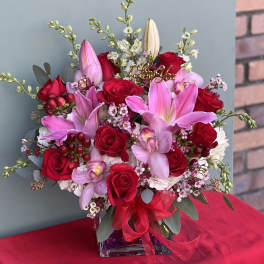 Bouquet of red roses and pink lilies in a glass vase with a ribbon