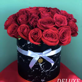 Red roses arranged in a black round box with a white ribbon