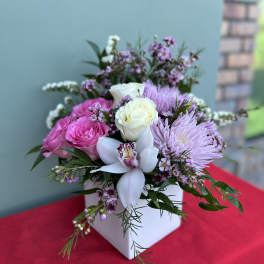 Pink and white floral arrangement in a white box with an orchid