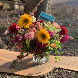 Mixed bouquet with sunflowers, roses, and orchids in a glass vase