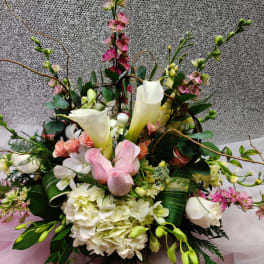 Low centerpiece of white calla lilies, hydrangeas, and pink roses with branches on a soft pink and silver backdrop