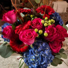 Bouquet of pink roses, red gerberas, and blue hydrangeas in a glass vase