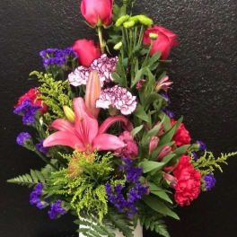Tall mixed bouquet in a white vase with pink roses, lilies, and purple accents