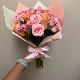 Handheld bouquet of pink and peach roses wrapped in pastel paper with a pink ribbon