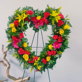 Heart-shaped floral wreath on a stand with red, yellow, and pink flowers
