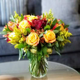 Bouquet of yellow roses and red flowers in a clear glass vase
