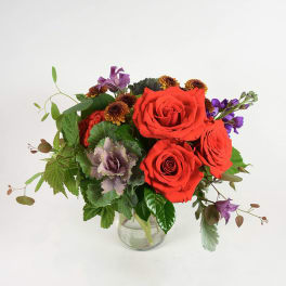 Red roses and purple flowers in a clear glass vase