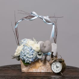 Hydrangea and rose arrangement in a birch box with a knitted elephant and alarm clock
