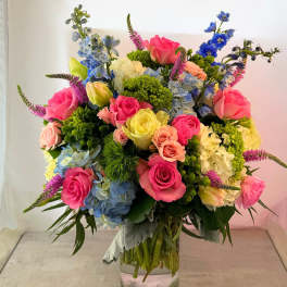 Colorful mixed bouquet in a clear glass vase with roses, hydrangeas, and blue flowers