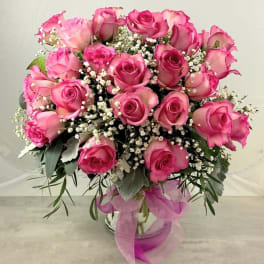 Pink roses arranged in a glass vase with baby's breath and ribbon