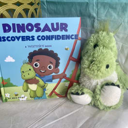 Children's dinosaur book beside a green plush dinosaur toy
