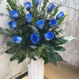 Blue roses in a tall white vase with mixed greenery