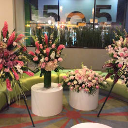 Four pink floral arrangements displayed on stands and pedestals in a lobby