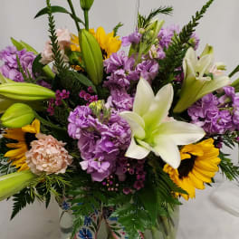 Mixed bouquet with lilies, sunflowers, and purple blooms in a glass vase