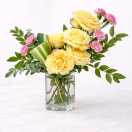 Yellow roses and pink carnations in a clear rectangular glass vase on a light surface