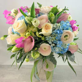 Bouquet of pastel roses, ranunculus, hydrangeas, and calla lilies in a glass vase
