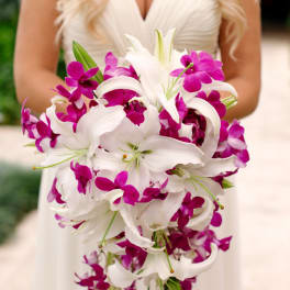Bride holding a cascading bouquet of white lilies and magenta orchids