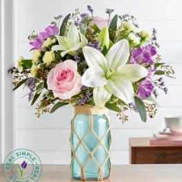 Pink rose and white lily bouquet in a blue glass vase