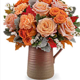 Orange and peach rose bouquet in a brown pitcher vase