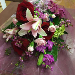 Bouquet of red roses, pink lilies, and purple flowers wrapped in clear cellophane
