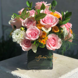 Pink and yellow rose arrangement in a dark square vase