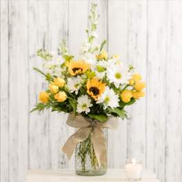 Yellow roses and white daisies in a glass vase with a burlap bow.
