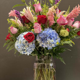 Mixed bouquet of roses, lilies, hydrangeas, and pink blooms in a glass vase