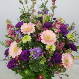 Mixed pink, purple, and green floral arrangement in a brown urn