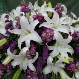 White lilies and purple flowers in a dense arrangement