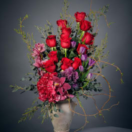 Tall bouquet of red roses, purple tulips, and pink orchids in a stone vase