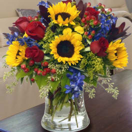 Bouquet of sunflowers, red roses, and blue flowers in a glass vase
