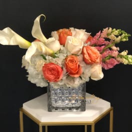 Bouquet of white calla lilies, coral roses, and pink snapdragons in a glass vase