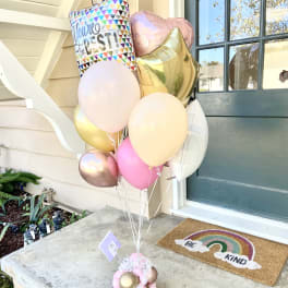 Cluster of pastel balloons with a "You're the Best" balloon and heart shapes by a front door