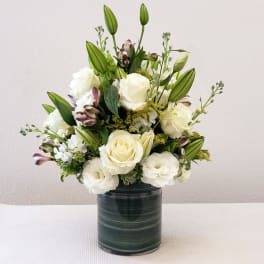 White roses and lilies arranged in a dark glass vase