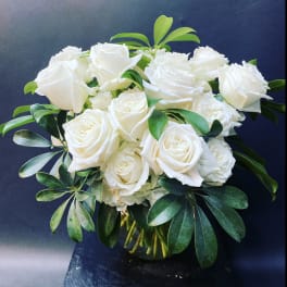 White roses arranged in a glass vase with green foliage
