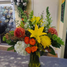 Bright mixed flower arrangement in a glass vase with yellow lilies and orange blooms