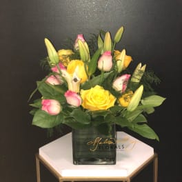 Yellow and pink roses with lily buds in a square glass vase