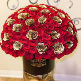 Large dome of red and gold roses arranged in a black hat box on a metallic pedestal