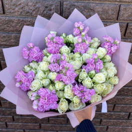 Hand-tied bouquet of cream spray roses and light lavender blooms wrapped in soft pink paper
